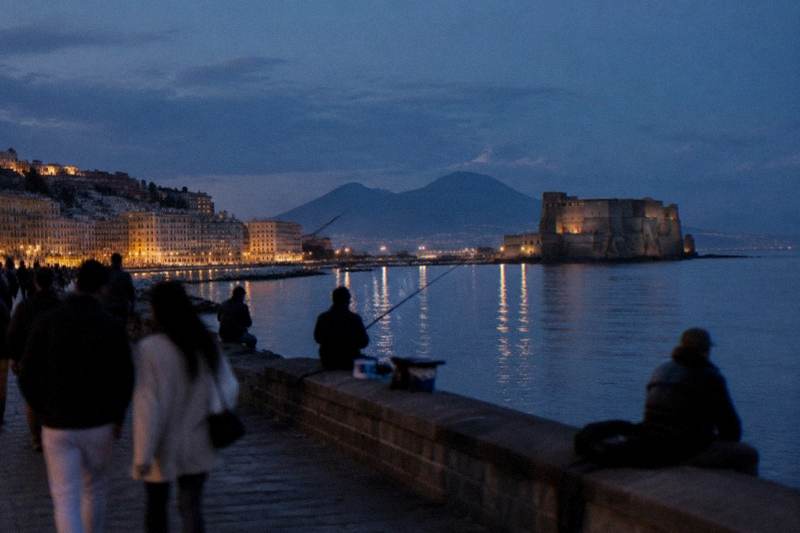 Strollers on the Naples sea wall at dusk with Vesuvius across the bay