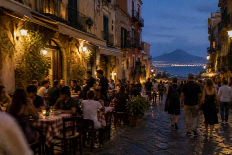 Pizzeria tables on a busy old-town street in Naples at evening