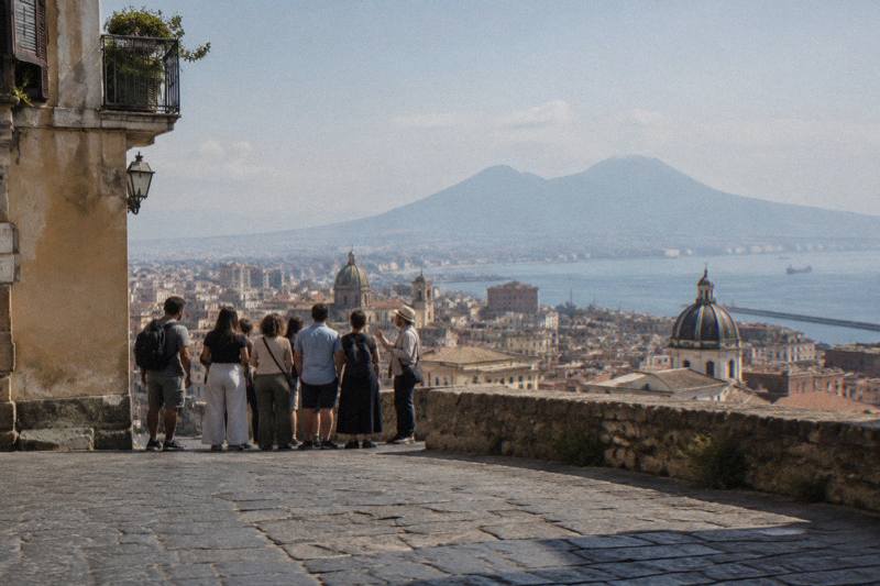 The old-town skyline of Naples with Vesuvius beyond the bay, with a small group of visitors