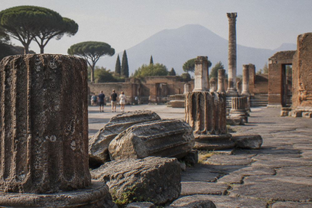 Rows of stone ruins and a preserved plaster cast display under a shelter at Pompeii