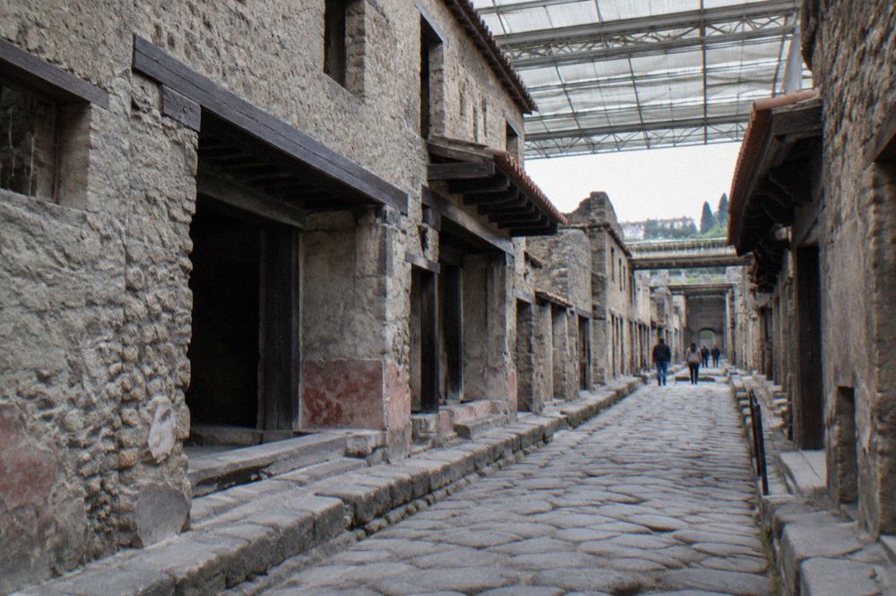 Ancient stone street in Herculaneum with brick walls and wooden beams preserved under a modern walkway