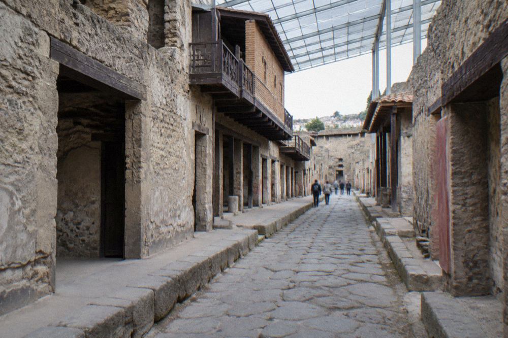 Excavated stone walls and columns of Herculaneum with modern Ercolano buildings visible above the ancient site