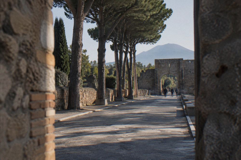 Row of broken columns and brick arches along a wide Pompeii street in warm afternoon light