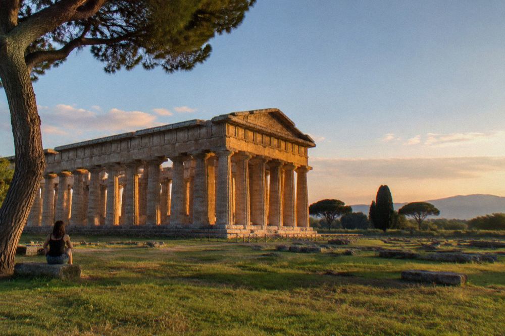Three ancient Greek temples standing in a grassy field under a wide sky