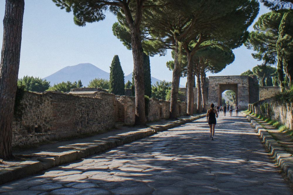 Ancient stone street in Pompeii with Mount Vesuvius rising in the distance under a clear sky
