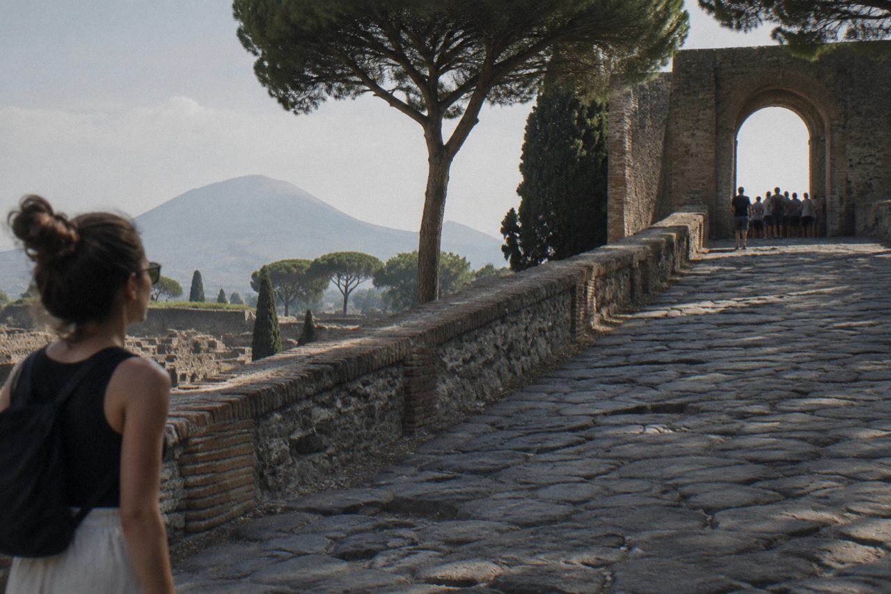 Parked cars along a tree-lined street beside the old stone walls of the Pompeii excavations