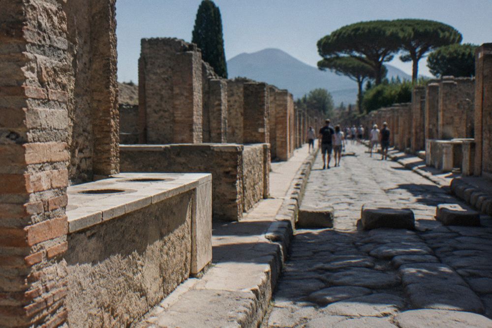 Phallic symbol carved into a stone paving block on an ancient Roman street in Pompeii with ruined walls on either side