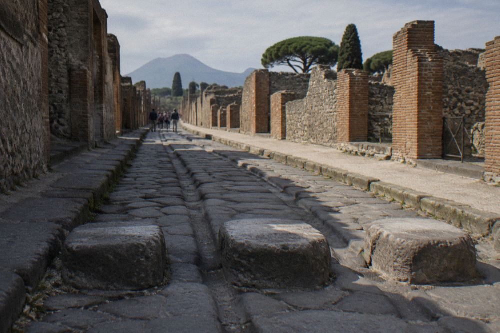 A quiet stone street in the excavated Roman city of Pompeii with Vesuvius rising behind it