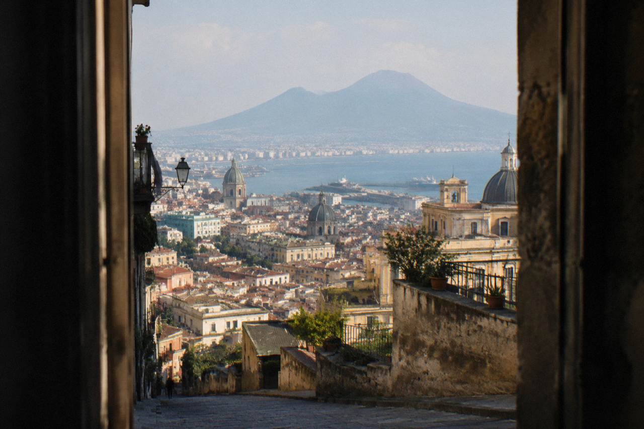 The Roman forum of Pompeii with stone columns and Mount Vesuvius rising in the background under a clear sky