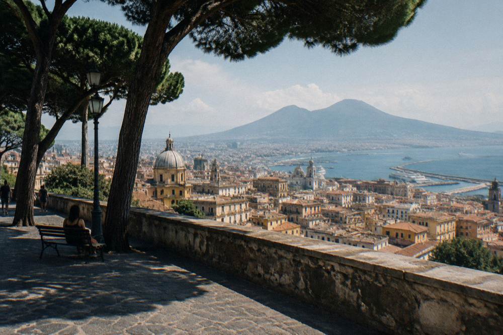 A panoramic view of Naples with Mount Vesuvius in the background and the Bay of Naples under a clear sky.