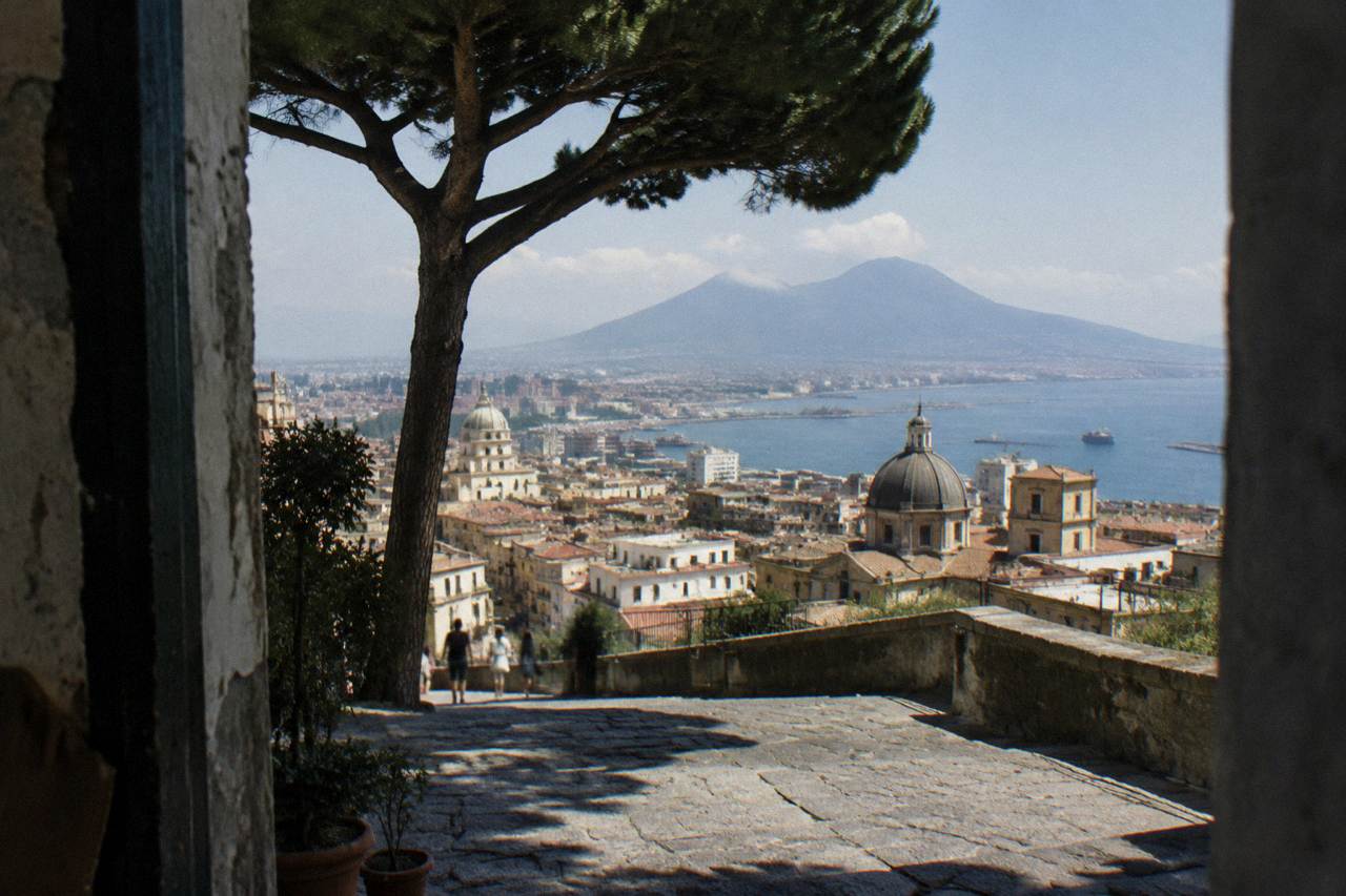 A panoramic view of Naples with Mount Vesuvius in the background and the Bay of Naples under a clear sky.