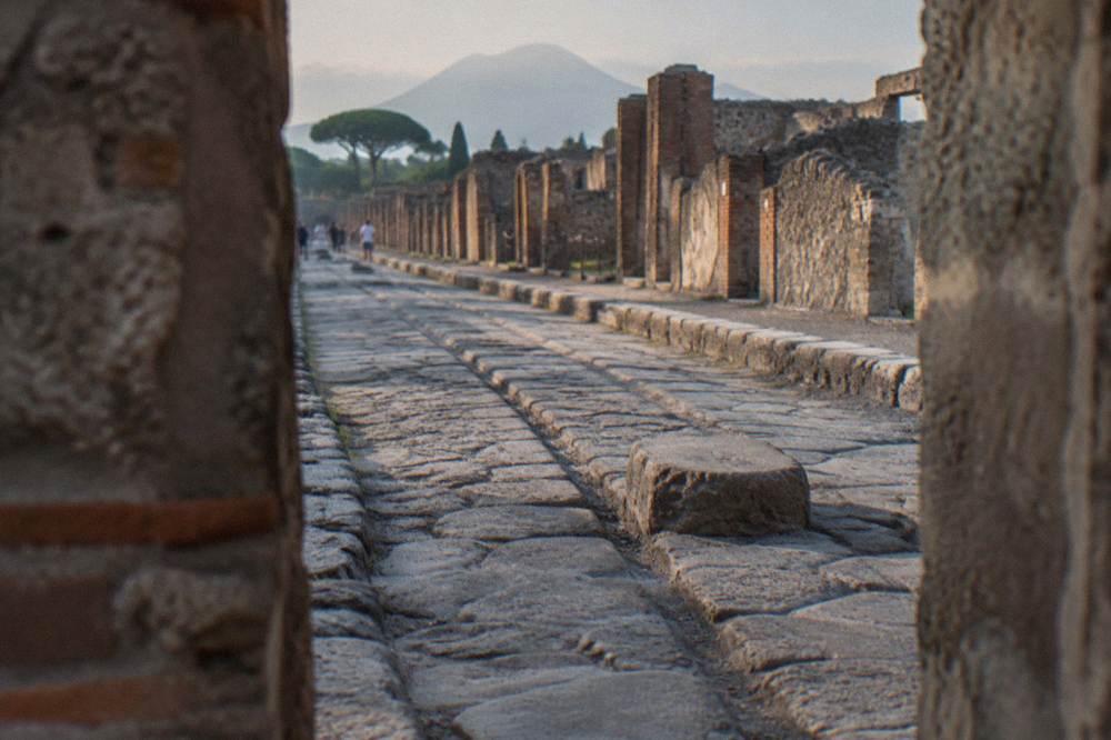 A quiet walkway through the excavated stone streets of the ancient Roman city of Pompeii under a pale sky