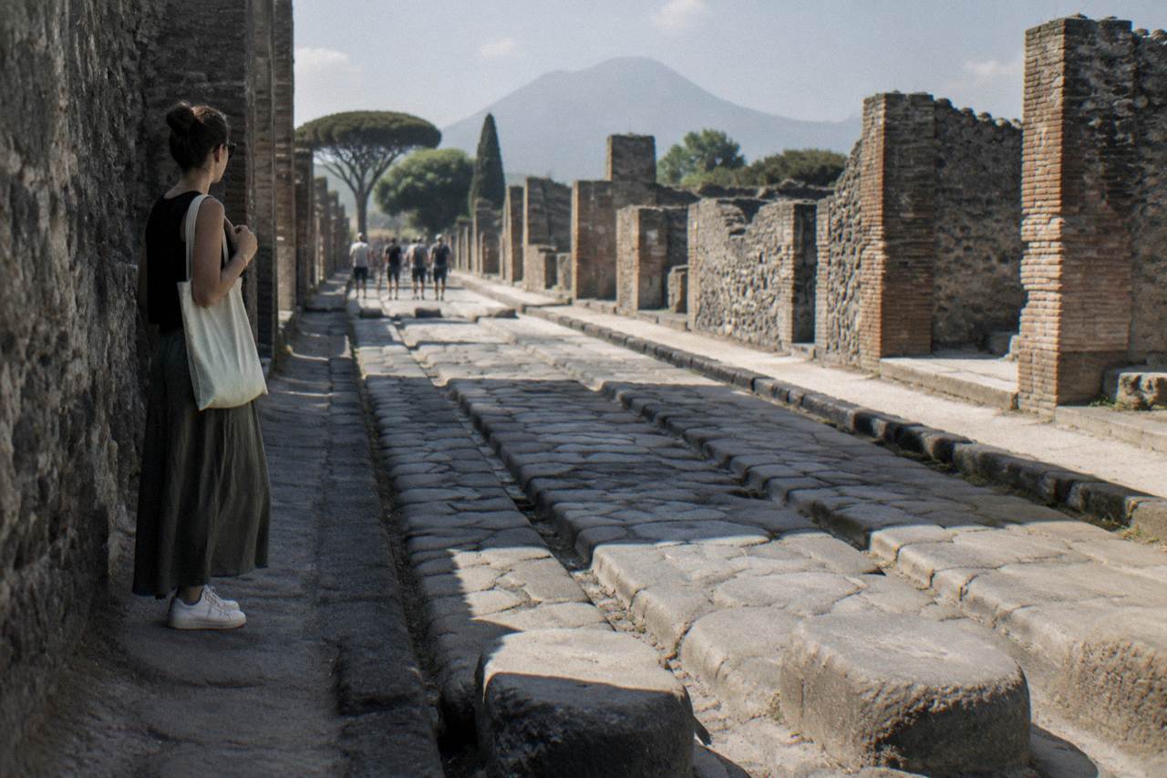 A quiet walkway through the excavated stone streets of the ancient Roman city of Pompeii under a pale sky