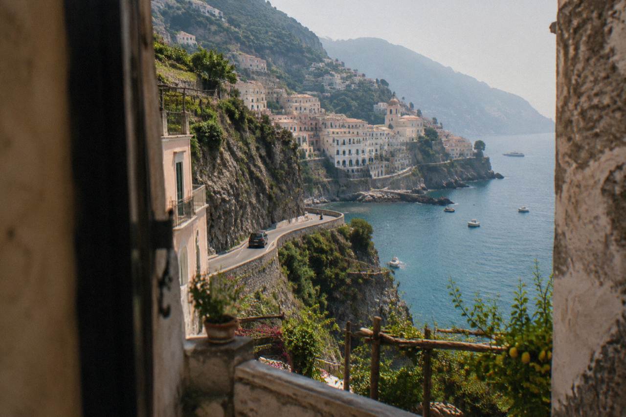 A pastel-coloured cliffside town above a blue bay with small boats moored along the shore