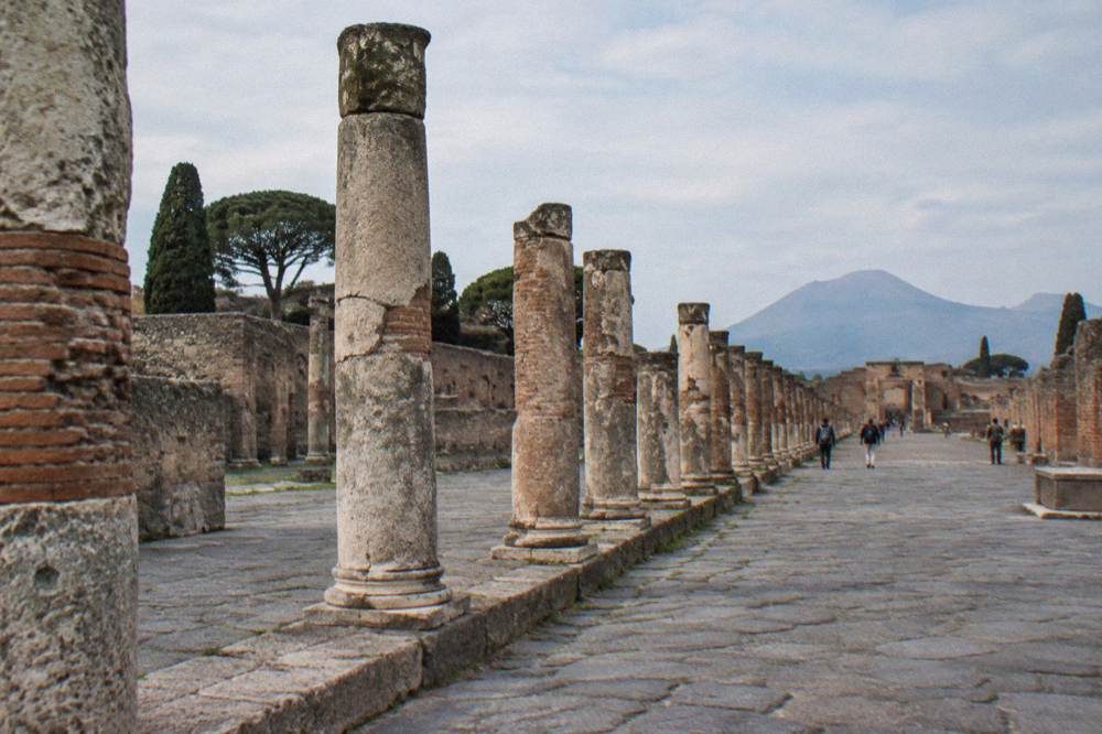 Empty stone street in Pompeii with worn stepping stones and ancient walls under a bright sky