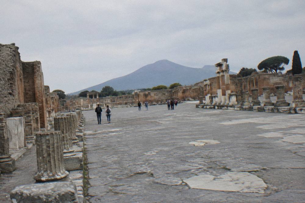 Weathered plaster casts of eruption victims displayed on a low shelf inside a dim Pompeii enclosure