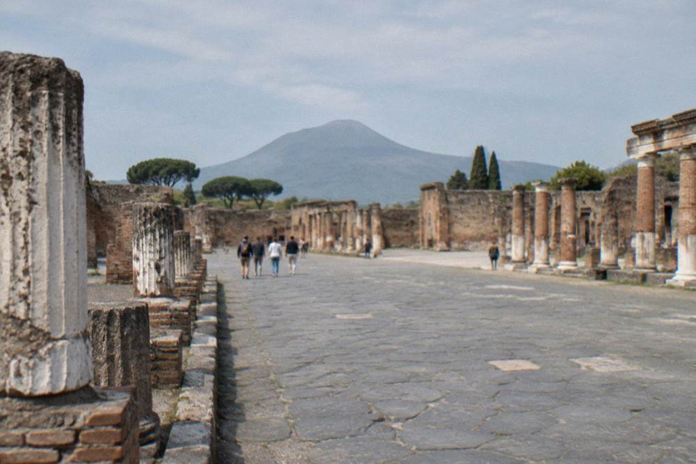Ancient stone walls and a narrow paved street inside the archaeological site of Pompeii under a clear sky