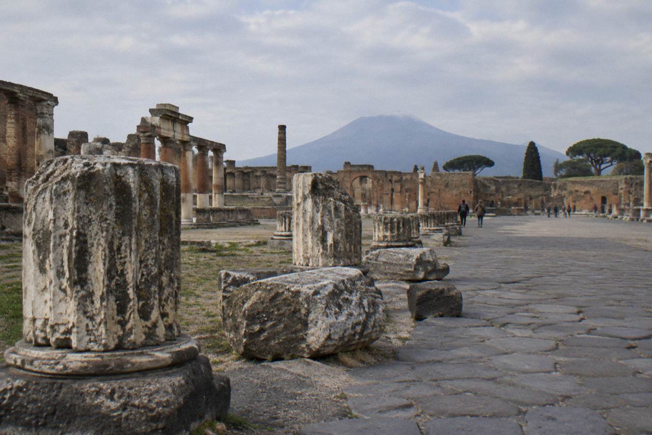 Ancient stone walls and a narrow paved street inside the archaeological site of Pompeii under a clear sky