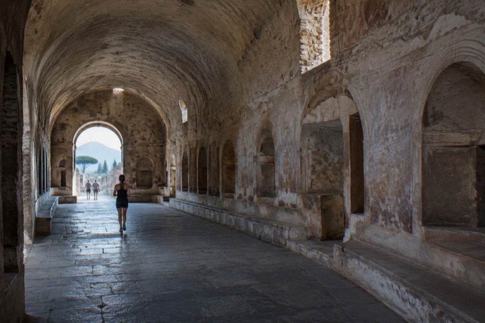 Vaulted stone bathing hall with arched light wells casting daylight onto ancient floors