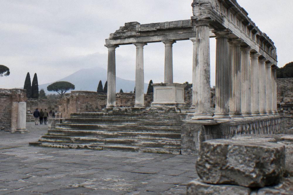 Ancient Roman street in Pompeii under strong midday sun with long stone walls and few shadows