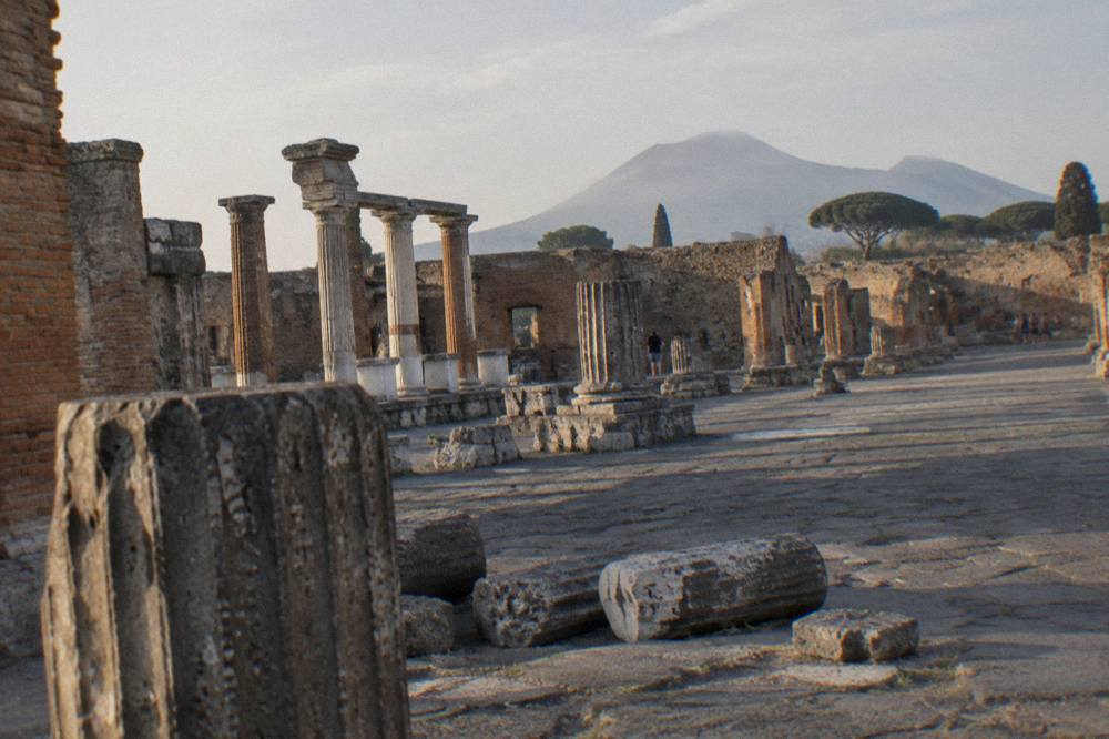 Stone columns and a paved street inside the ruins of Pompeii leading towards the open forum area in warm morning light
