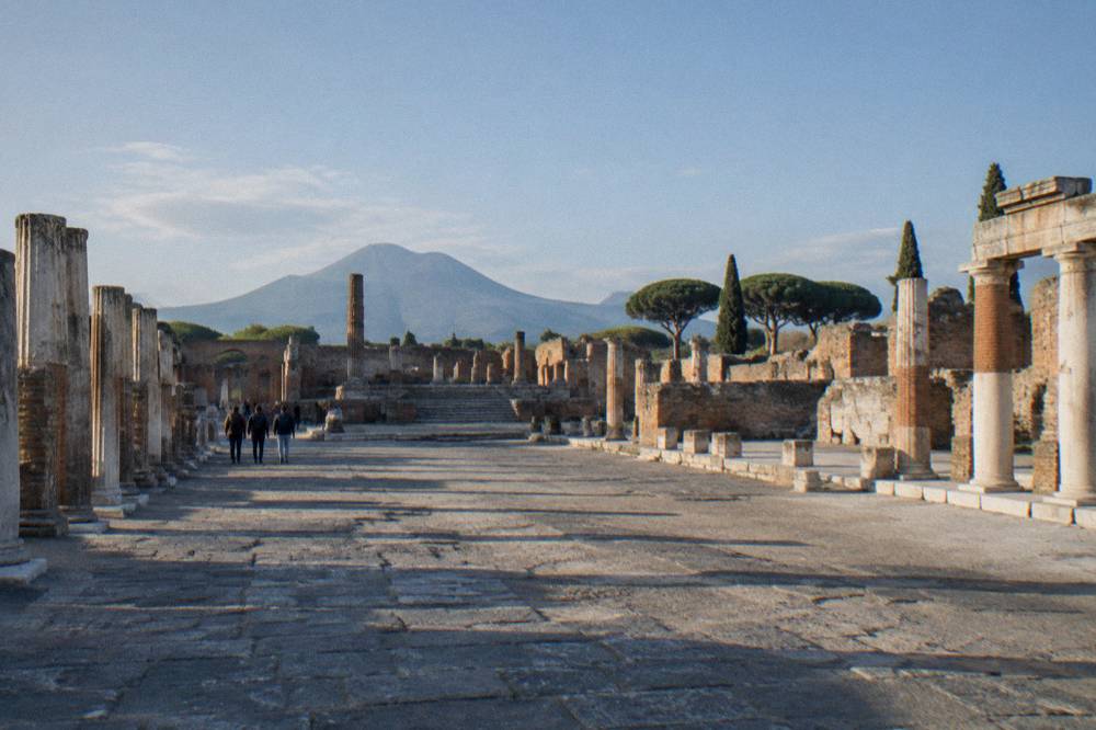 Early morning light across the empty forum square of Pompeii with long shadows from stone columns and Mount Vesuvius rising behind