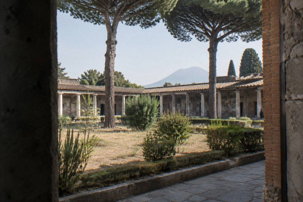 A small group of visitors standing among ancient stone columns while a guide gestures towards the ruined buildings around the forum square
