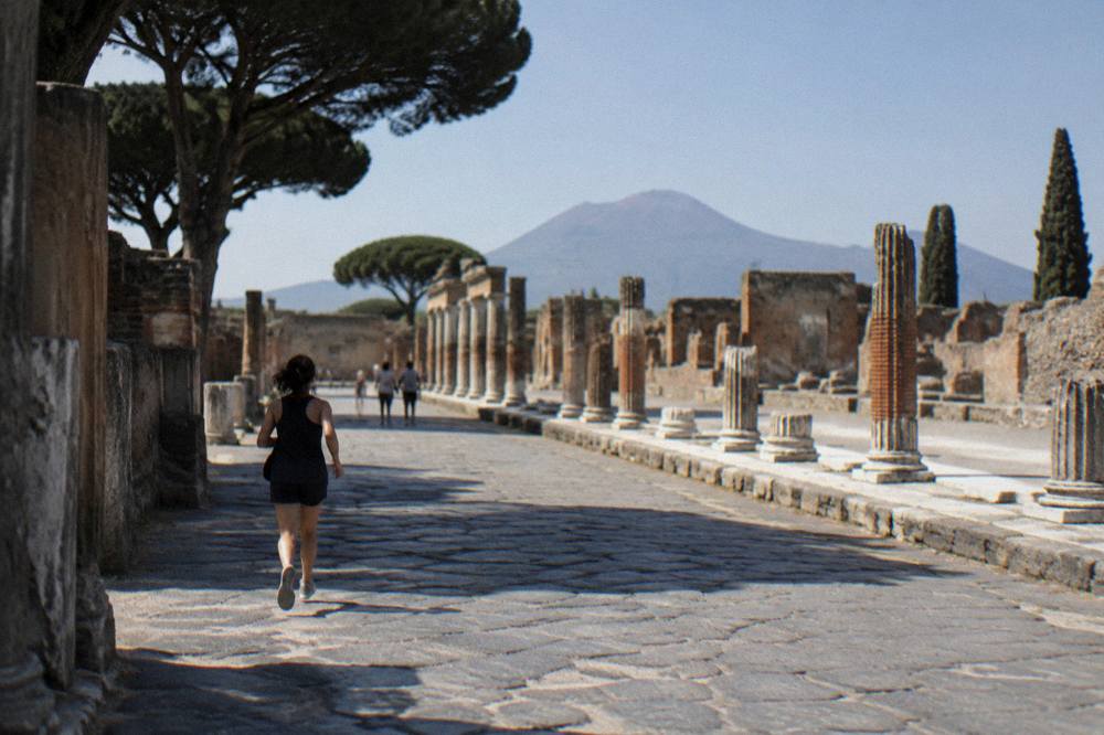 A paved ancient street in Pompeii receding towards distant ruins, with worn stone wheel ruts and high stone stepping stones crossing the surface