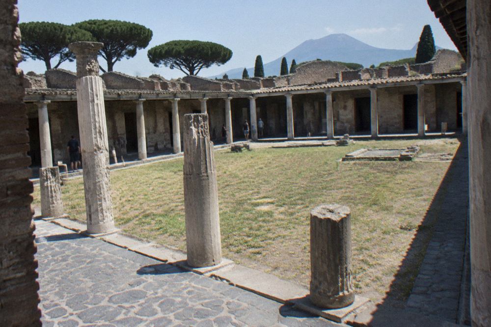 Stone arcade surrounding an open grassed courtyard within the ruins of Pompeii