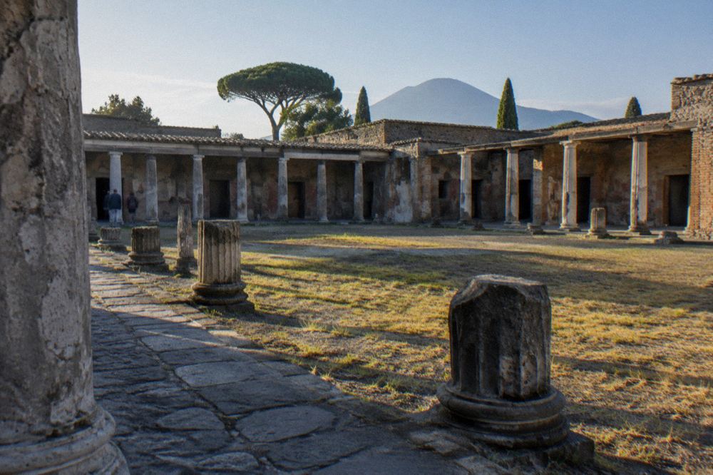 Sunlit stone-paved street in Pompeii lined by low ruined walls under a clear sky