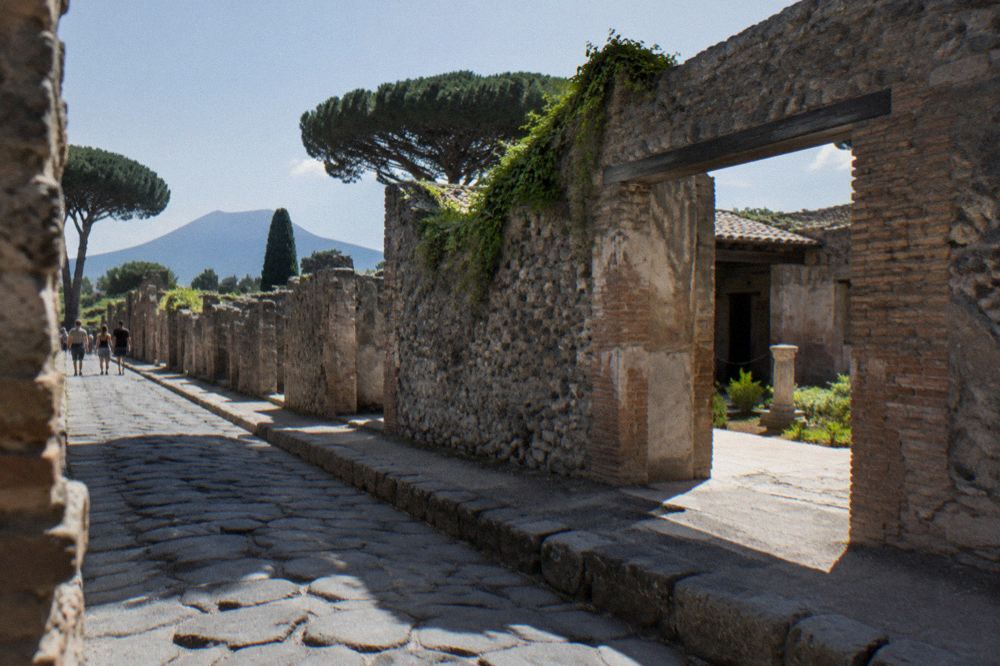Long excavated Roman street in Pompeii receding toward a city gate in daylight