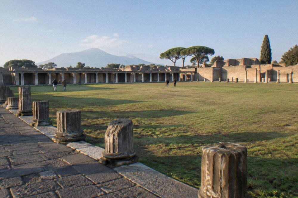 A long colonnade of stone columns casting morning shadows across a walkway beside an open field