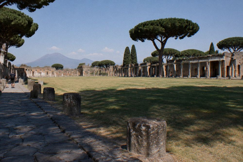 Late afternoon light across a broad open court with columns on three sides and a distant volcano on the horizon