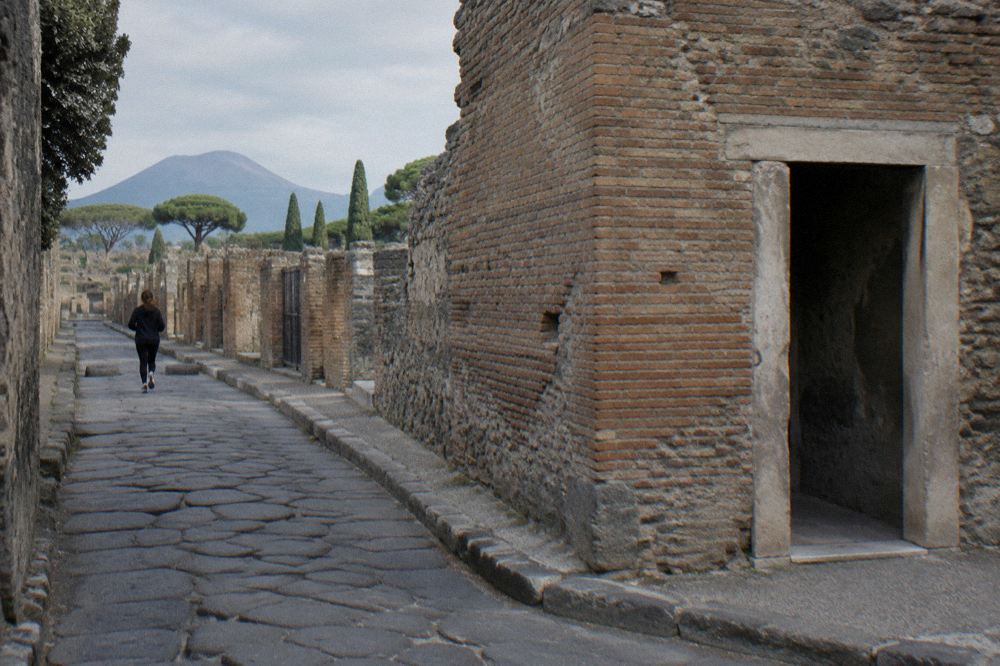 Wide view over the excavated rooftops and street grid of Pompeii toward Mount Vesuvius in the distance