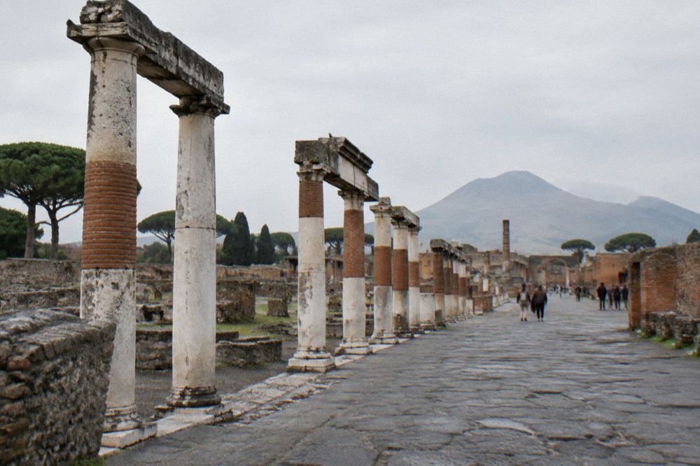 A guide speaking to a small group of visitors among ancient stone walls and columns at Pompeii