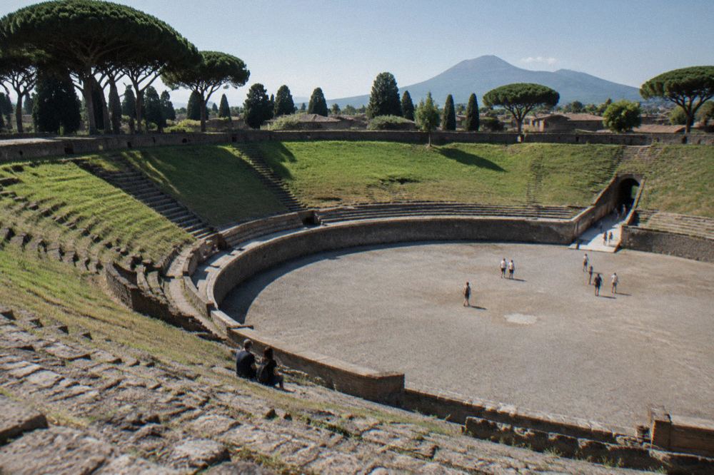 A stone gateway arch of the ancient arena at Pompeii opening onto a sunlit path