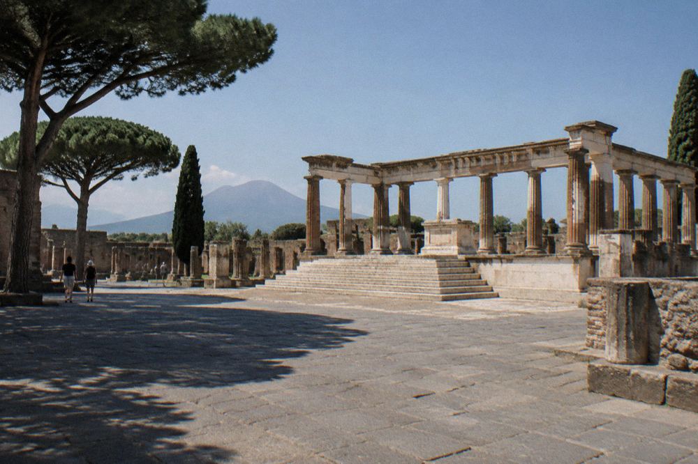 A weathered stone altar in the foreground with temple columns behind it on a raised platform