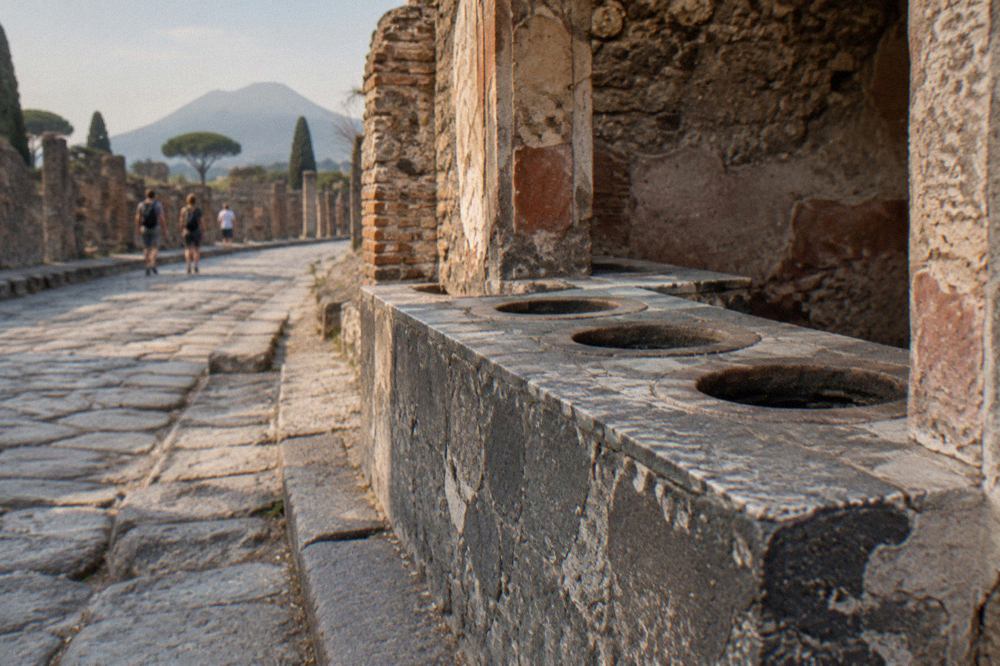 Ancient masonry counter with round clay jars set into its top beside a ruined Pompeii street