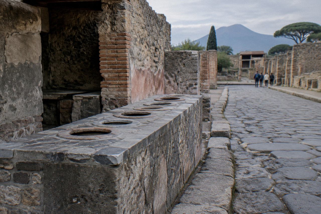 Ancient masonry counter with round clay jars set into its top beside a ruined Pompeii street