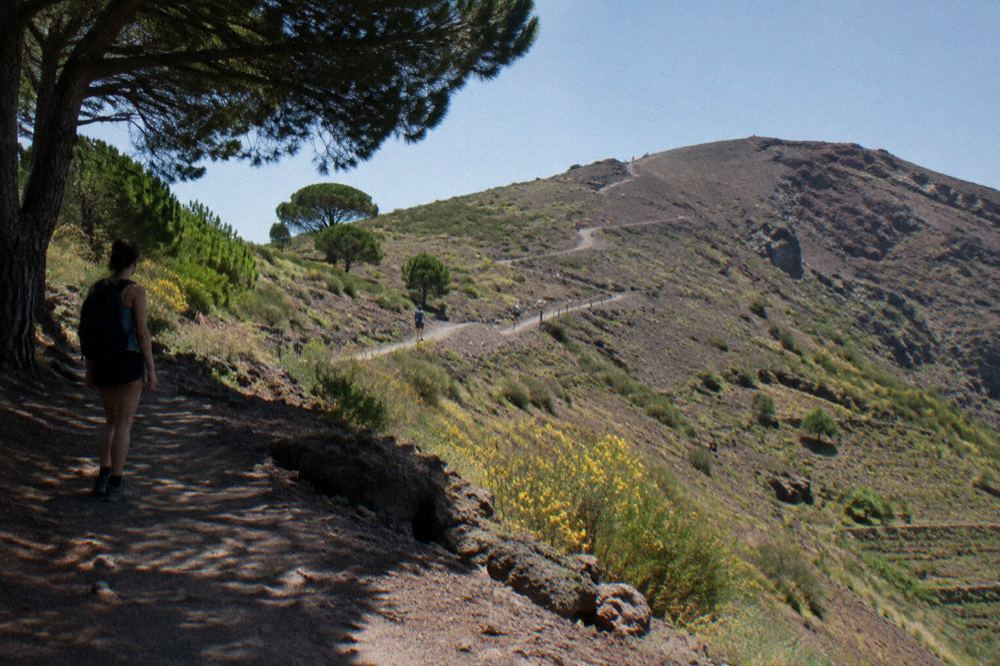 A winding mountain road climbing through scrubland toward the Vesuvius parking area