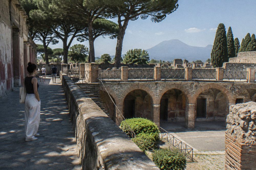 A long Roman villa building with plain walls standing beside an ancient stone road under a clear sky