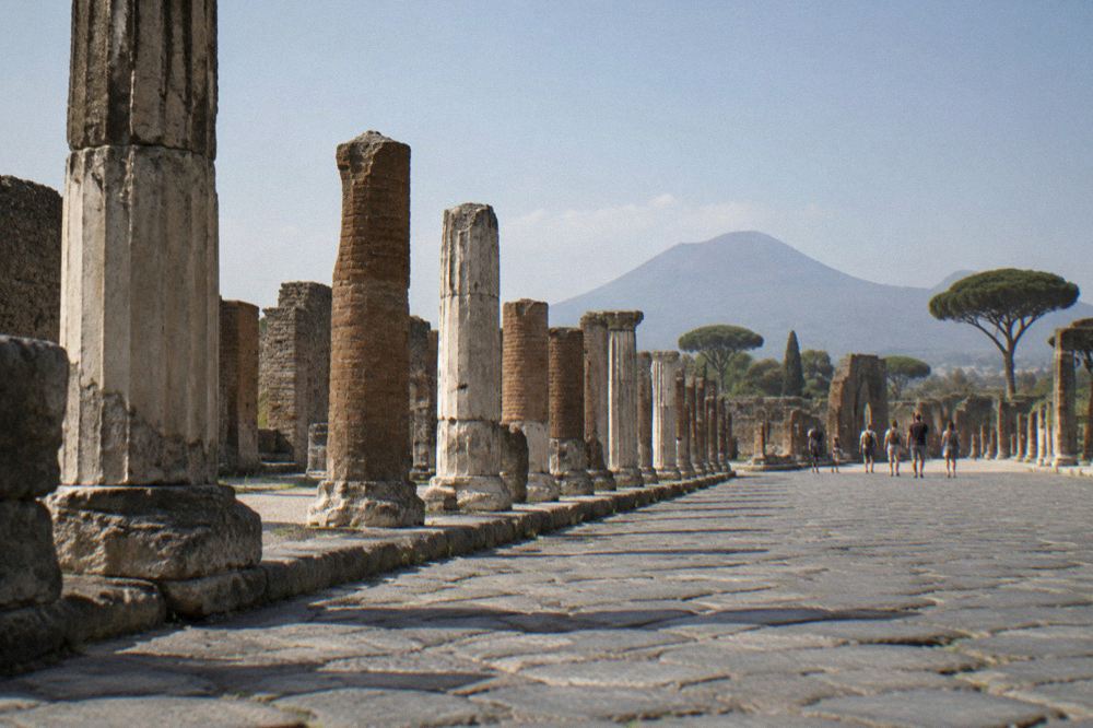 The exterior of a Roman villa at golden hour with long shadows across an ancient road