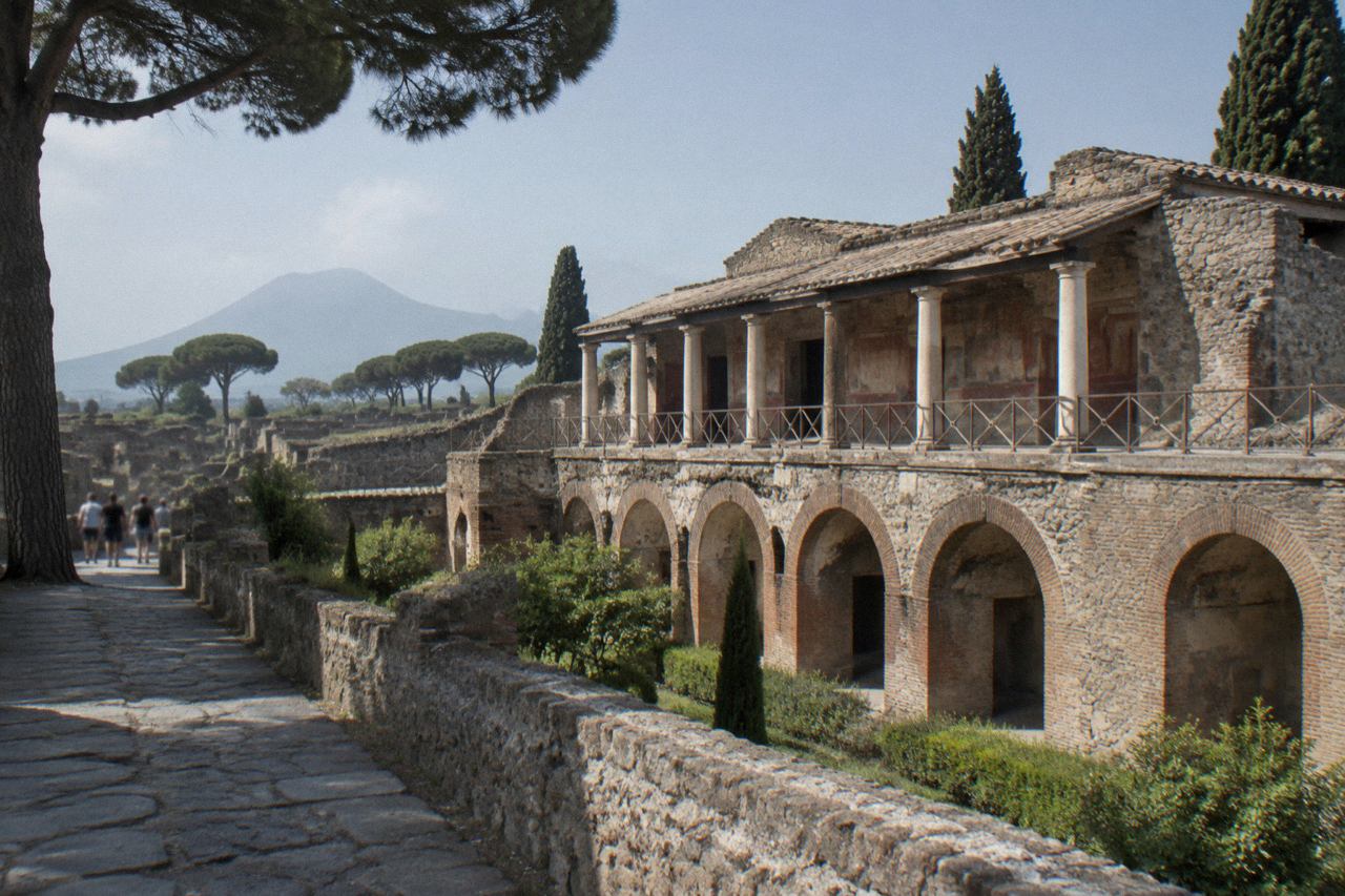 A long Roman villa building with plain walls standing beside an ancient stone road under a clear sky