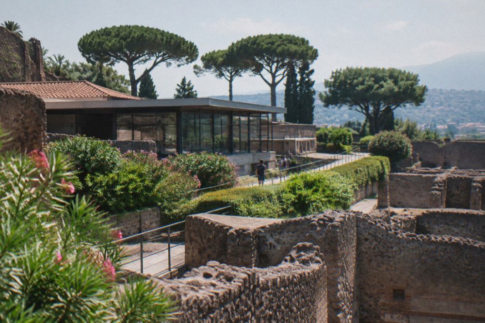 Terraced ruins of an ancient Roman villa on a slope above a plain, with a modern town and a mountain in the distance