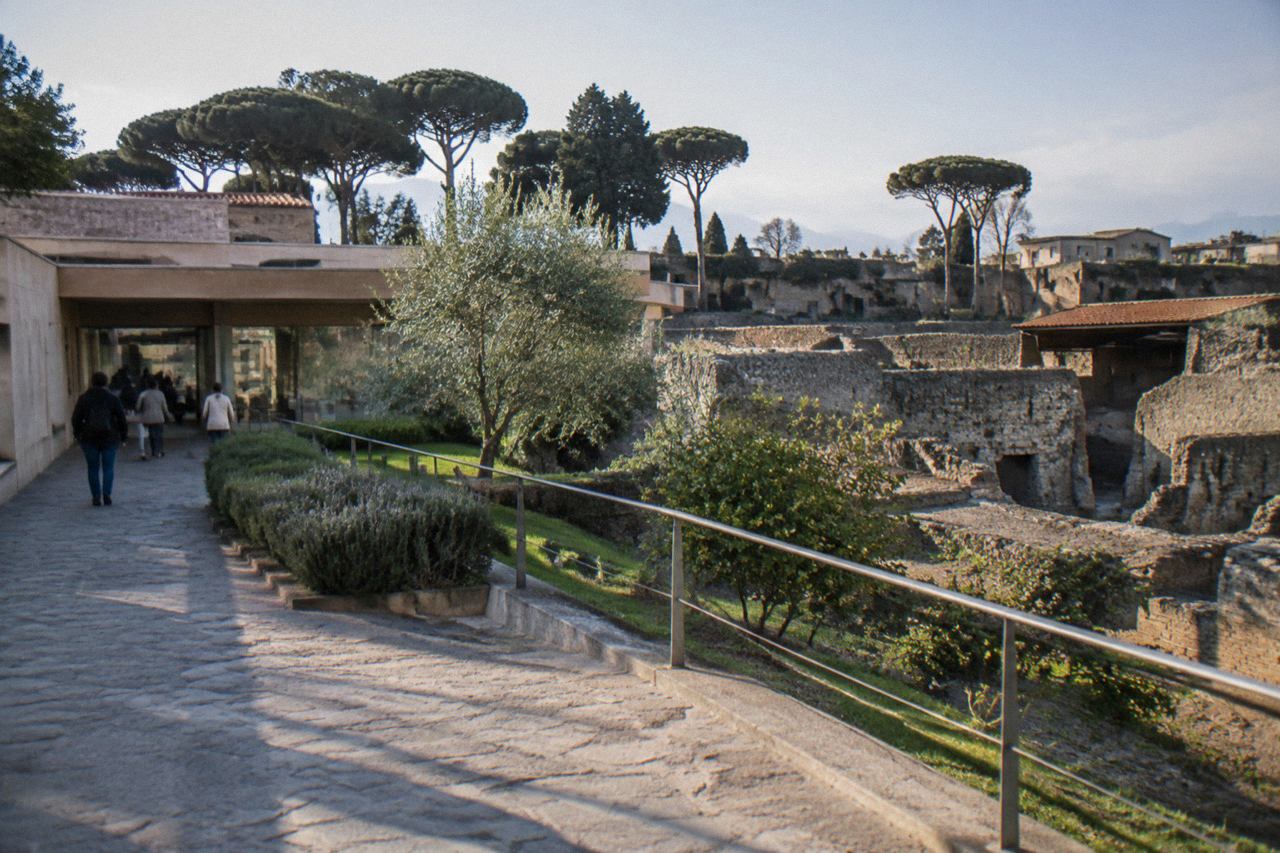 Terraced ruins of an ancient Roman villa on a slope above a plain, with a modern town and a mountain in the distance