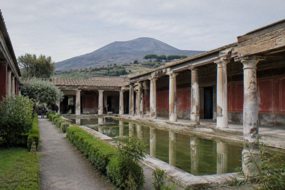 Sunlit excavated villa courtyard with low stone walls and green lawn in late afternoon light