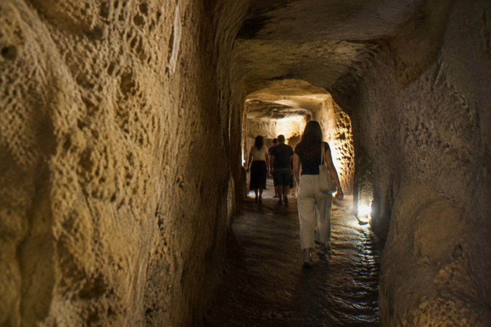 A stone staircase descending into a dim underground tunnel with arched brick walls