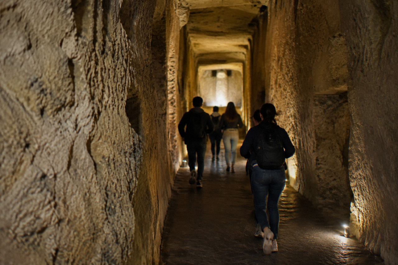 A stone staircase descending into a dim underground tunnel with arched brick walls