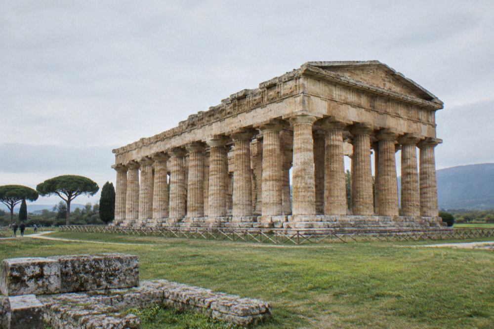 Three ancient Greek Doric temples standing in a grassy field under a wide sky