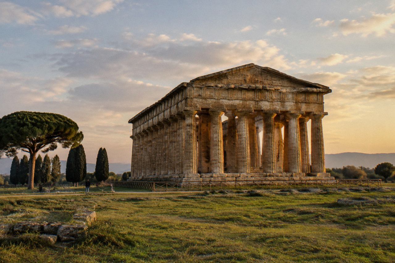Three ancient Greek Doric temples standing in a grassy field under a wide sky
